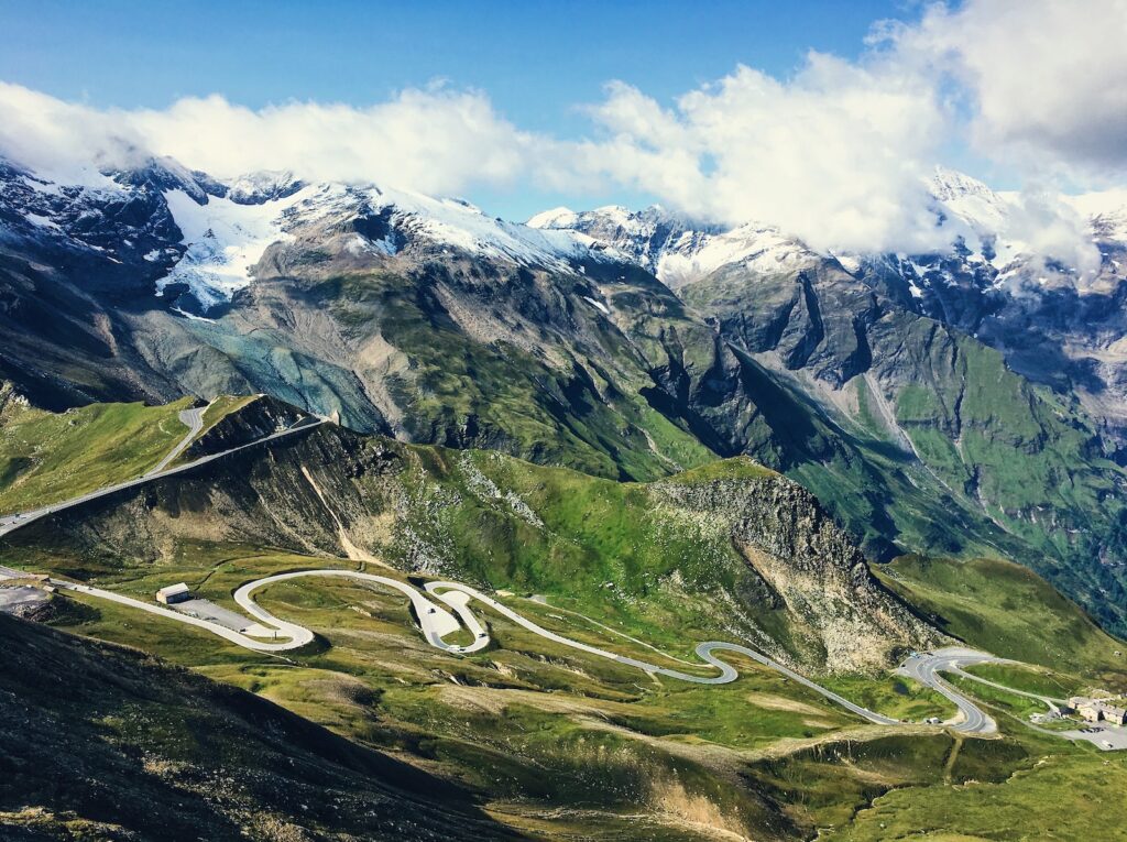 a winding road in the mountains with snow capped mountains in the background