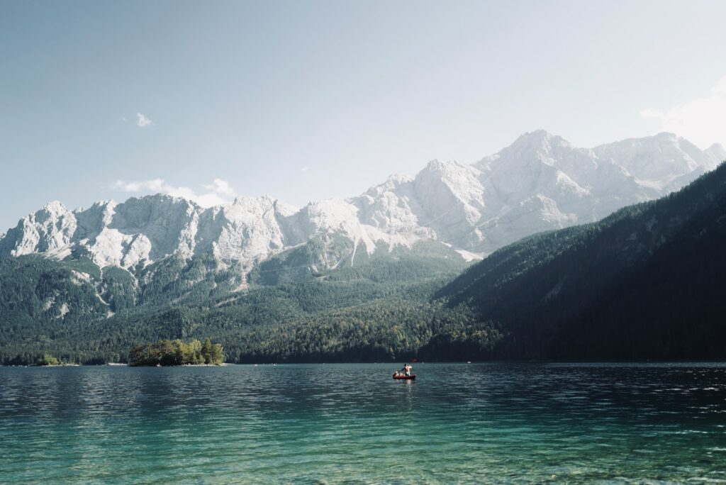 person in red shirt riding on boat on lake near mountain during daytime