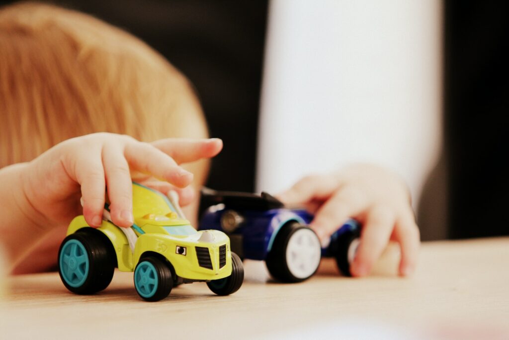 child playing with two assorted-color car plastic toys on brown wooden table