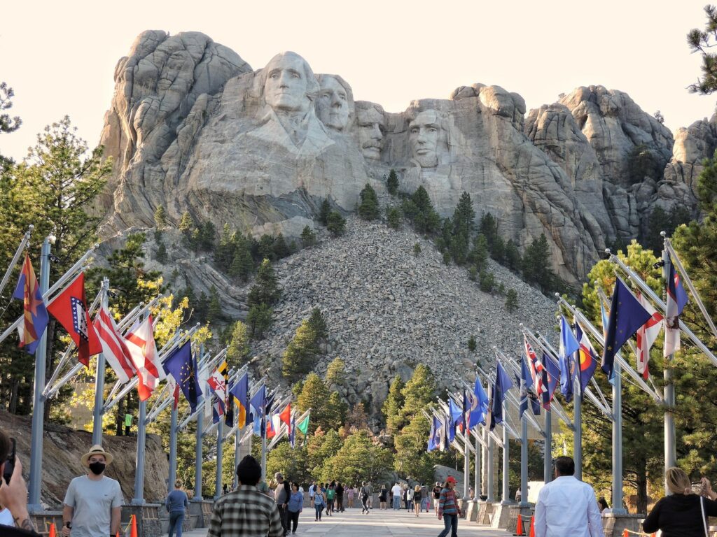 Rushmore a group of people walking on a path with flags and Mount Rushmore National Memorial in the background