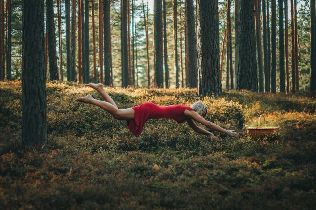 a woman in a red dress laying on the ground in a forest