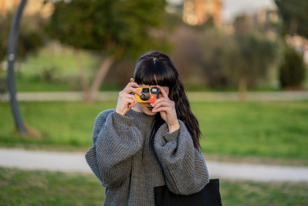 woman wearing gray knitted sweater holding yellow point-and-shoot camera